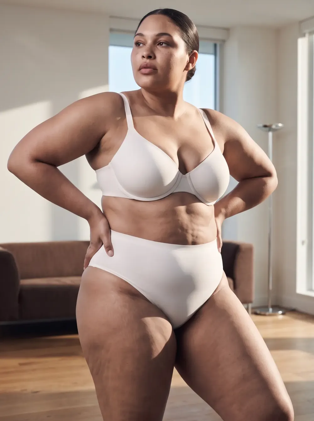 Donna in reggiseno e slip a vita alta chiari, mani sui fianchi in un soggiorno luminoso